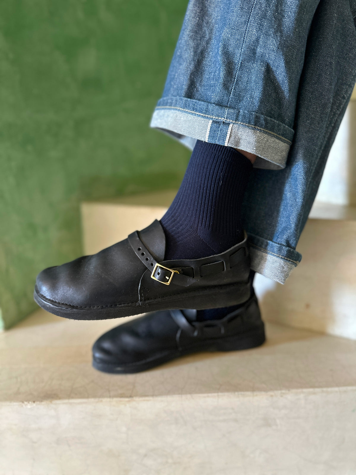 Lifestyle detail of black Aurora Middle English leather strap shoes styled with denim jeans and navy socks