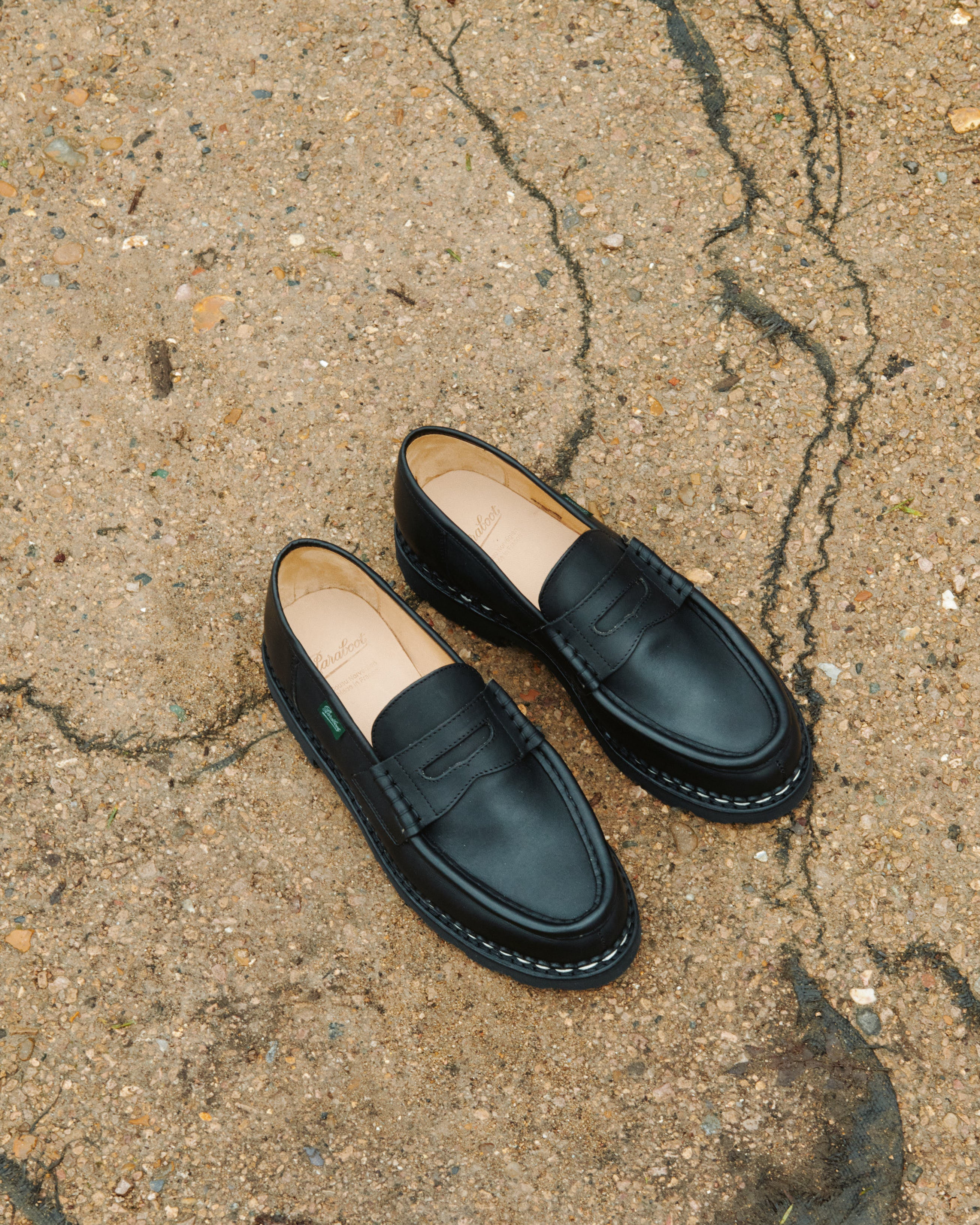 Lifestyle view of Paraboot Reims black lisse leather penny loafers on concrete surface
